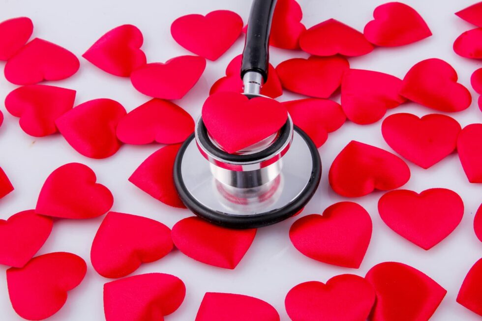A stethoscope placed on a red heart shape, surrounded by multiple red heart shapes scattered on a white surface.